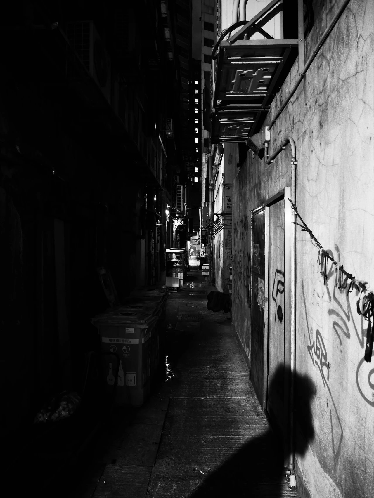 A person walking through a narrow alley in black and white.