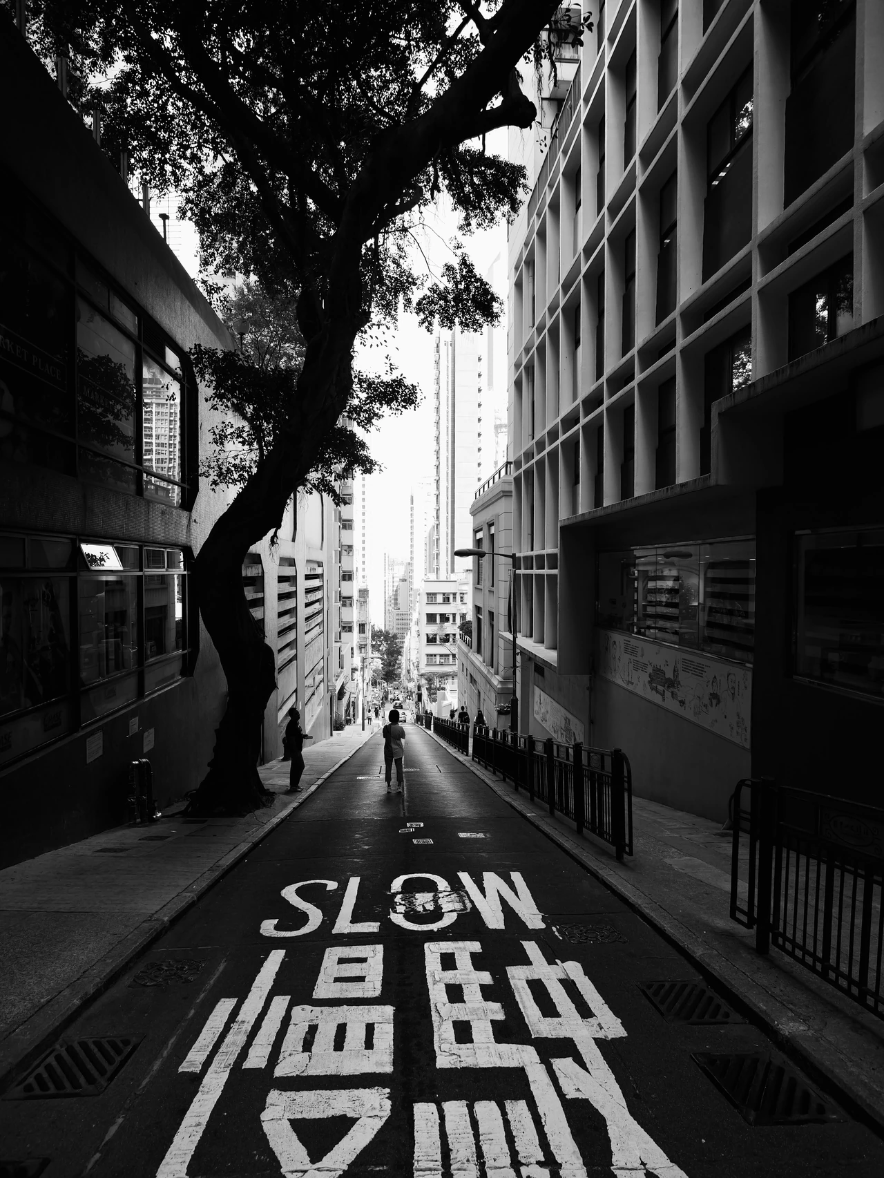 A narrow street marked SLOW in English and Chinese, in black and white.