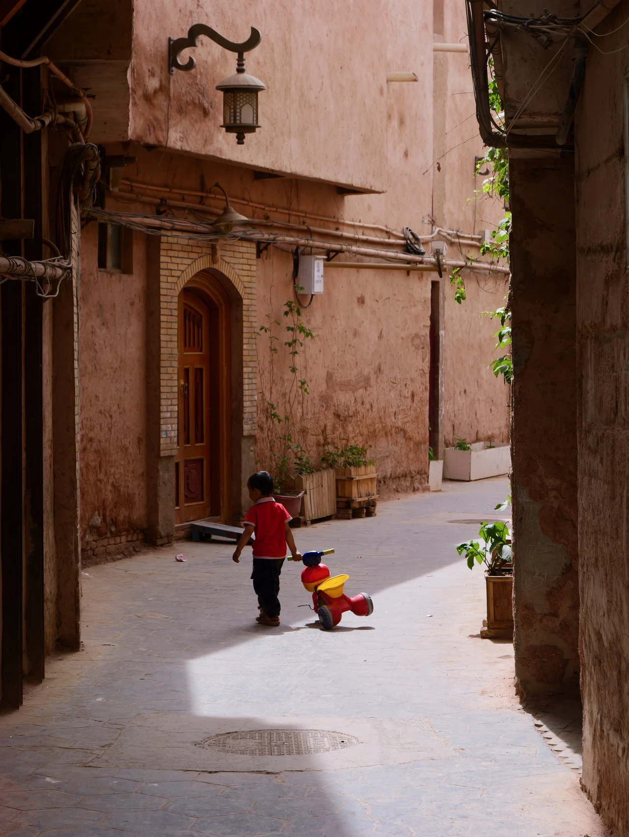 People in a sunlit street between warm-coloured buildings.