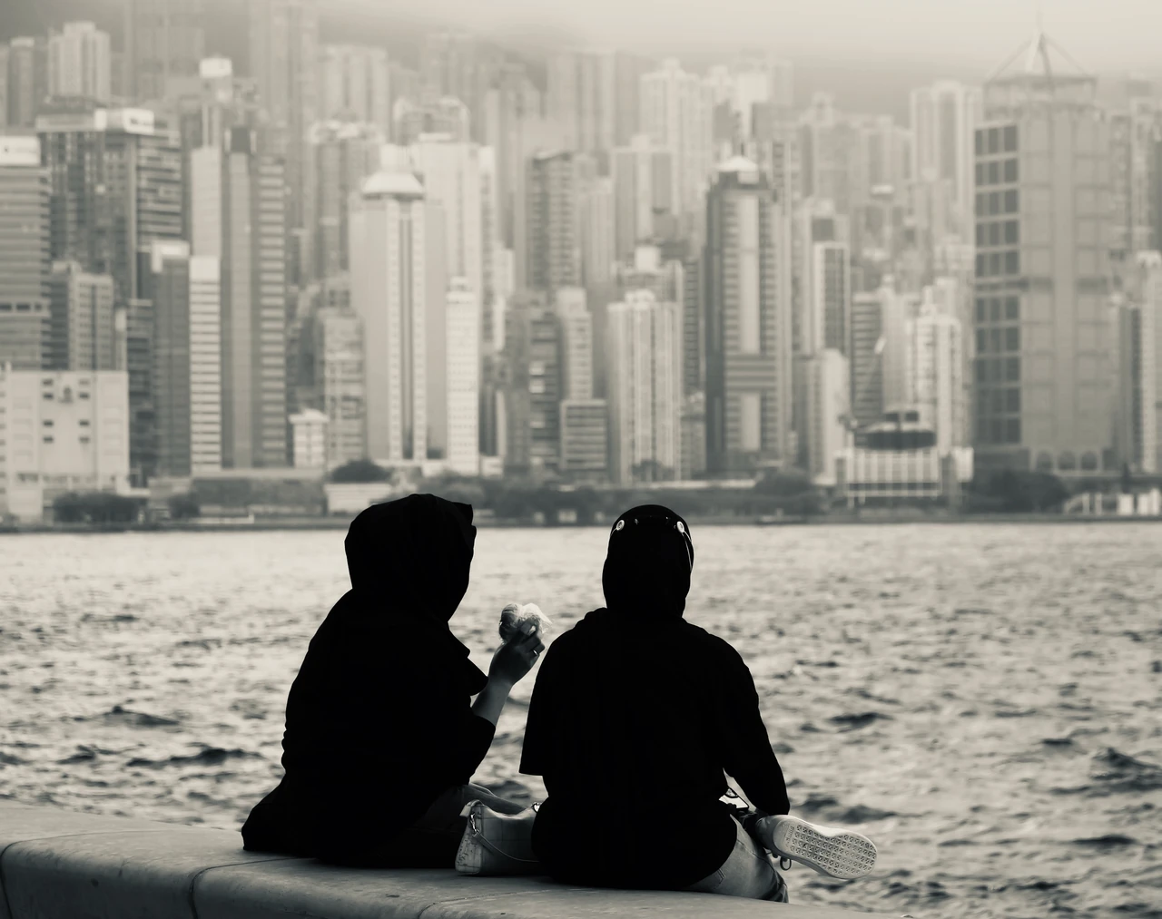 Two people silhouetted against a dense skyline across the water.