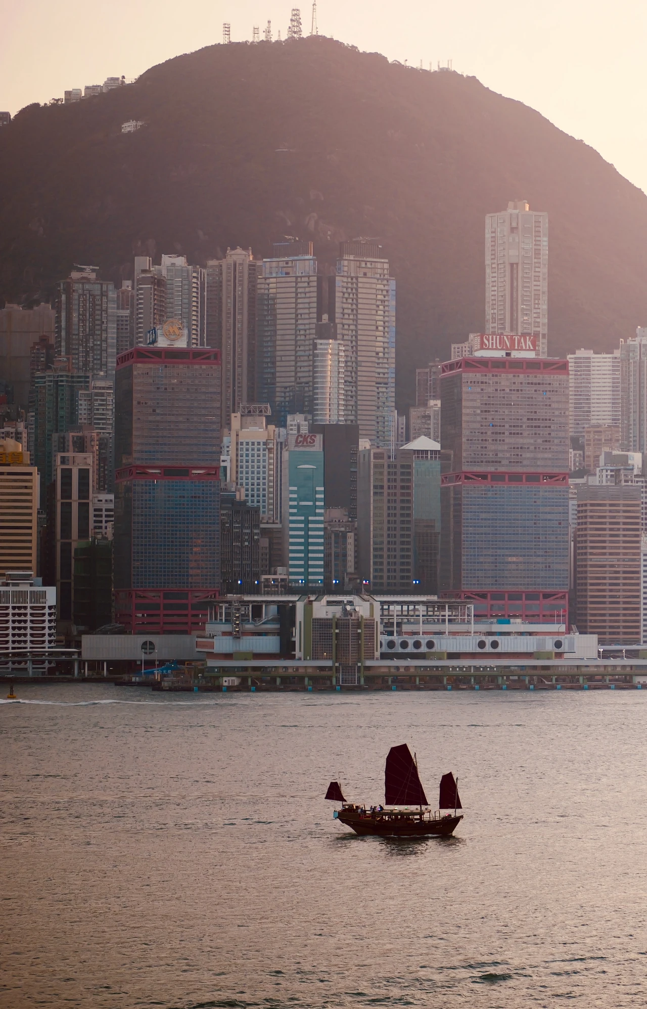 A small boat below densely built hills in warm evening light.