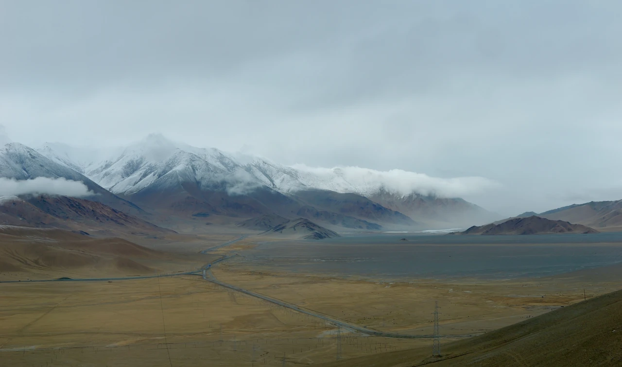 Open grassland beneath snowy mountains and low clouds.