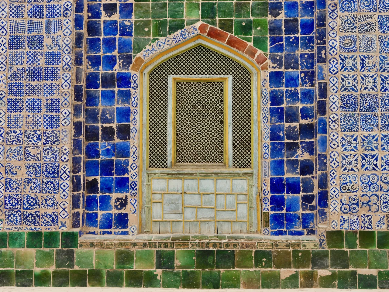 An ornate window surrounded by blue, yellow and green tiles.